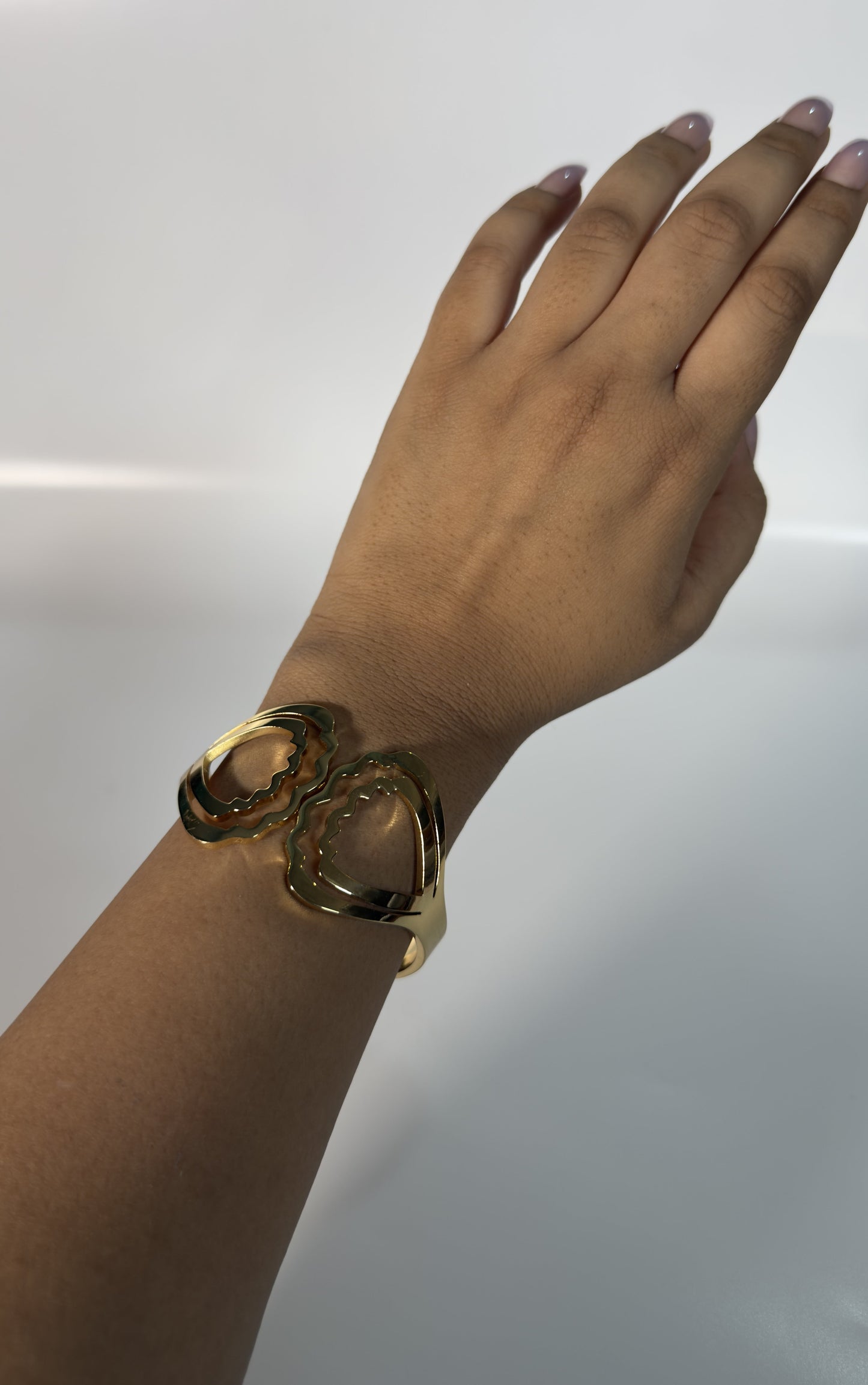 Gold bracelet on a wrist against a plain background