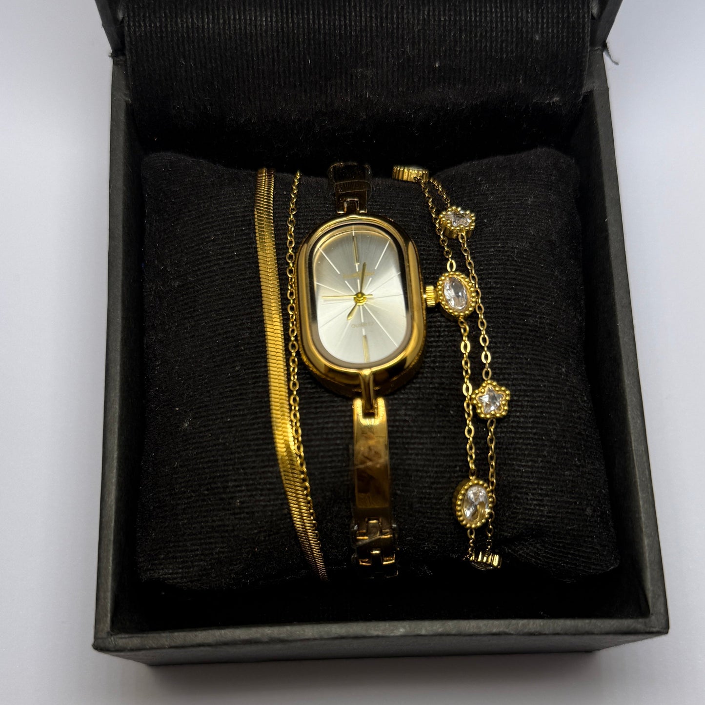Gold watch and bracelet set in a black box on a white background