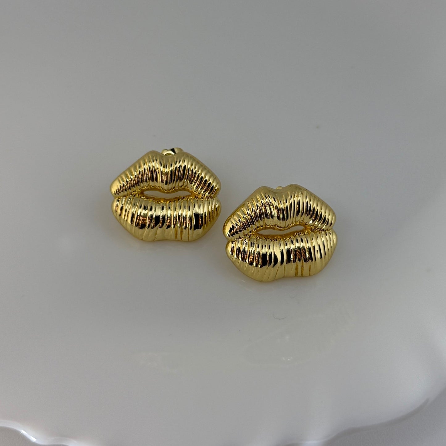 Gold lip-shaped earrings on a white shell