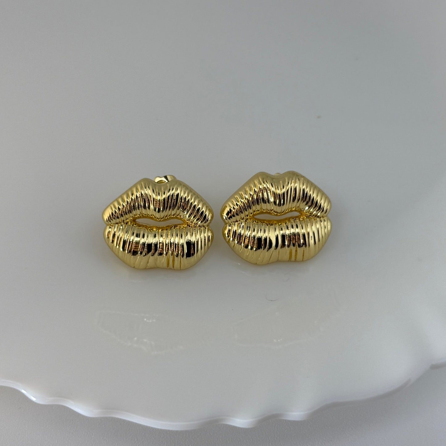 Gold lip-shaped earrings on a white dish