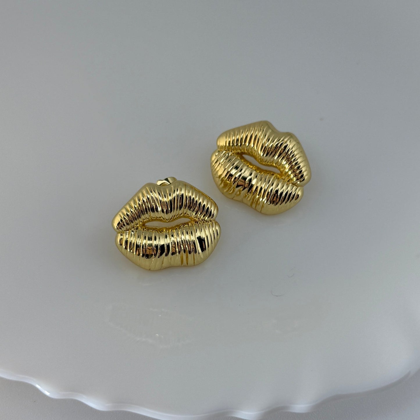 Gold lip-shaped earrings on a white dish