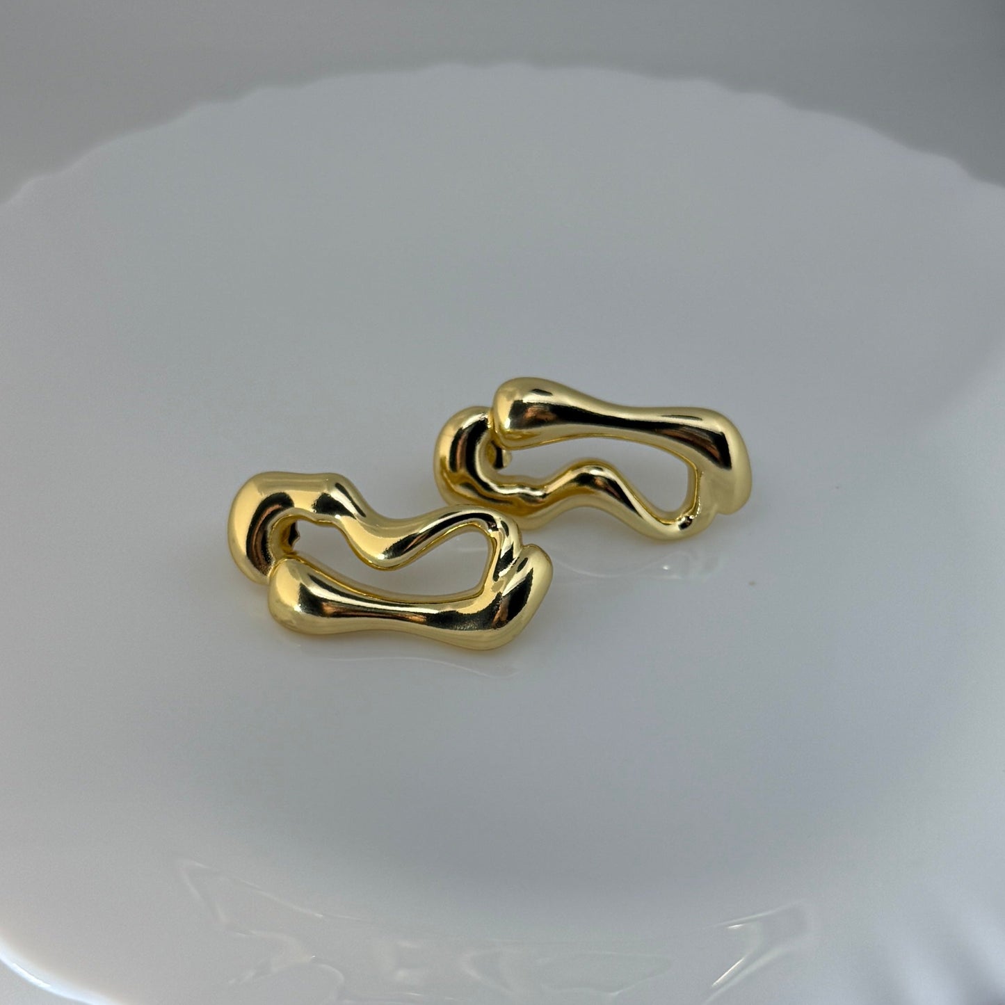 Gold chain-style earrings on a white dish