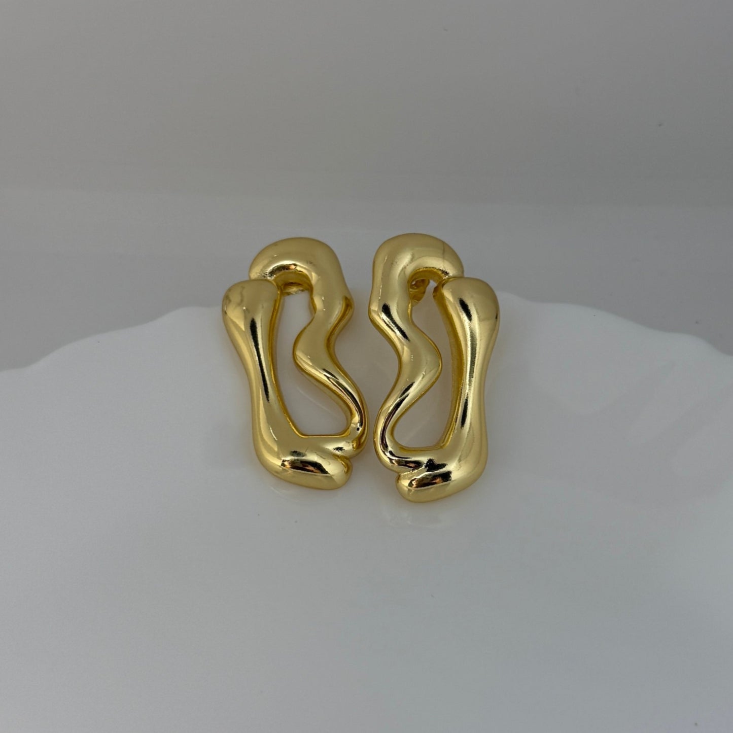 Pair of gold earrings on a white surface with a light gray background