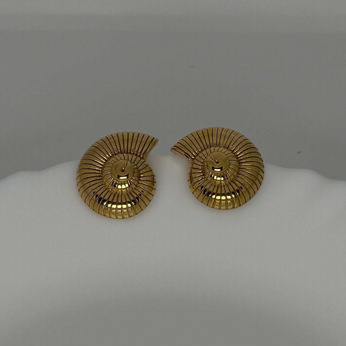Pair of gold earrings on a white mannequin bust against a gray background