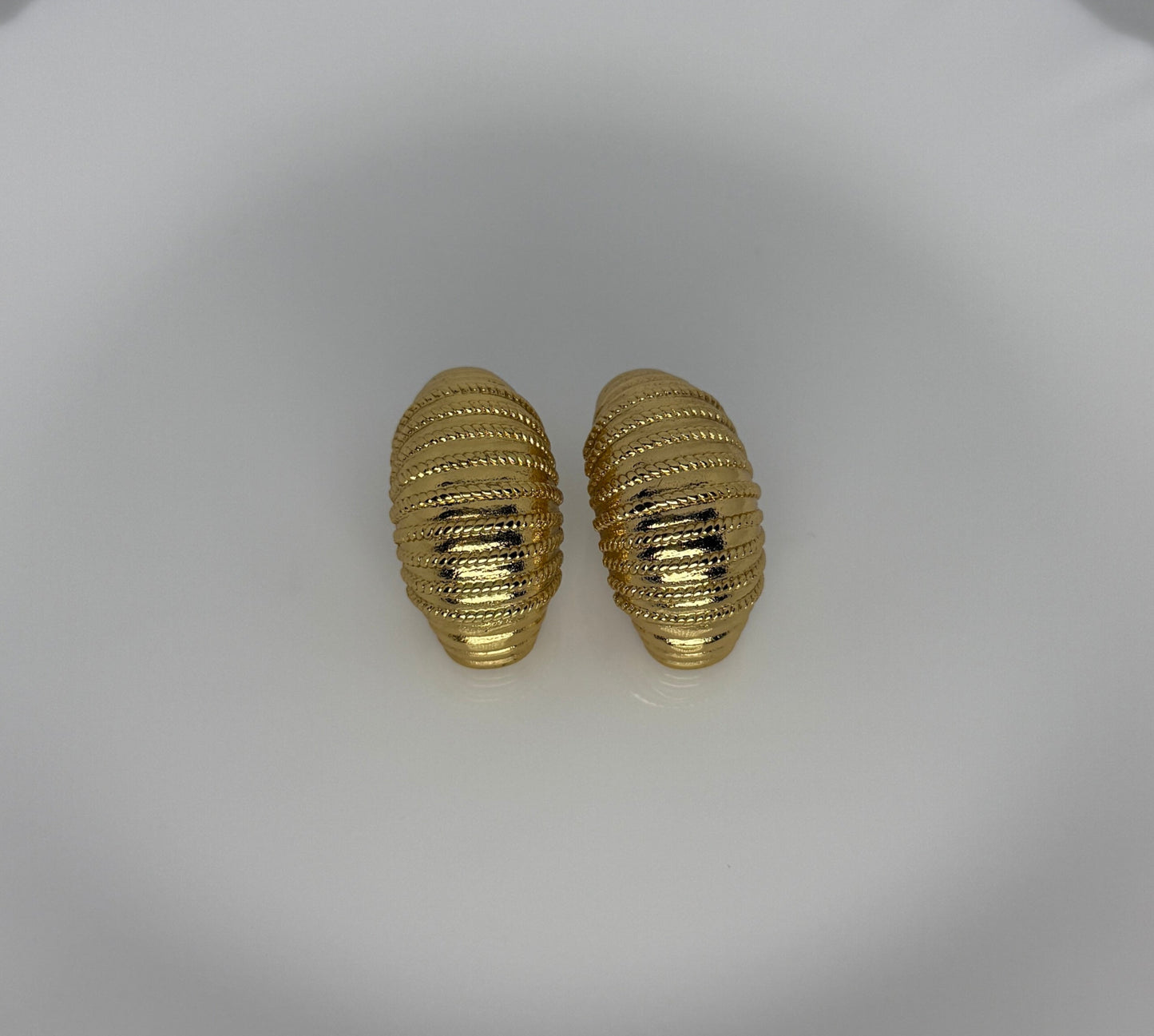 Pair of gold textured earrings on a white dish