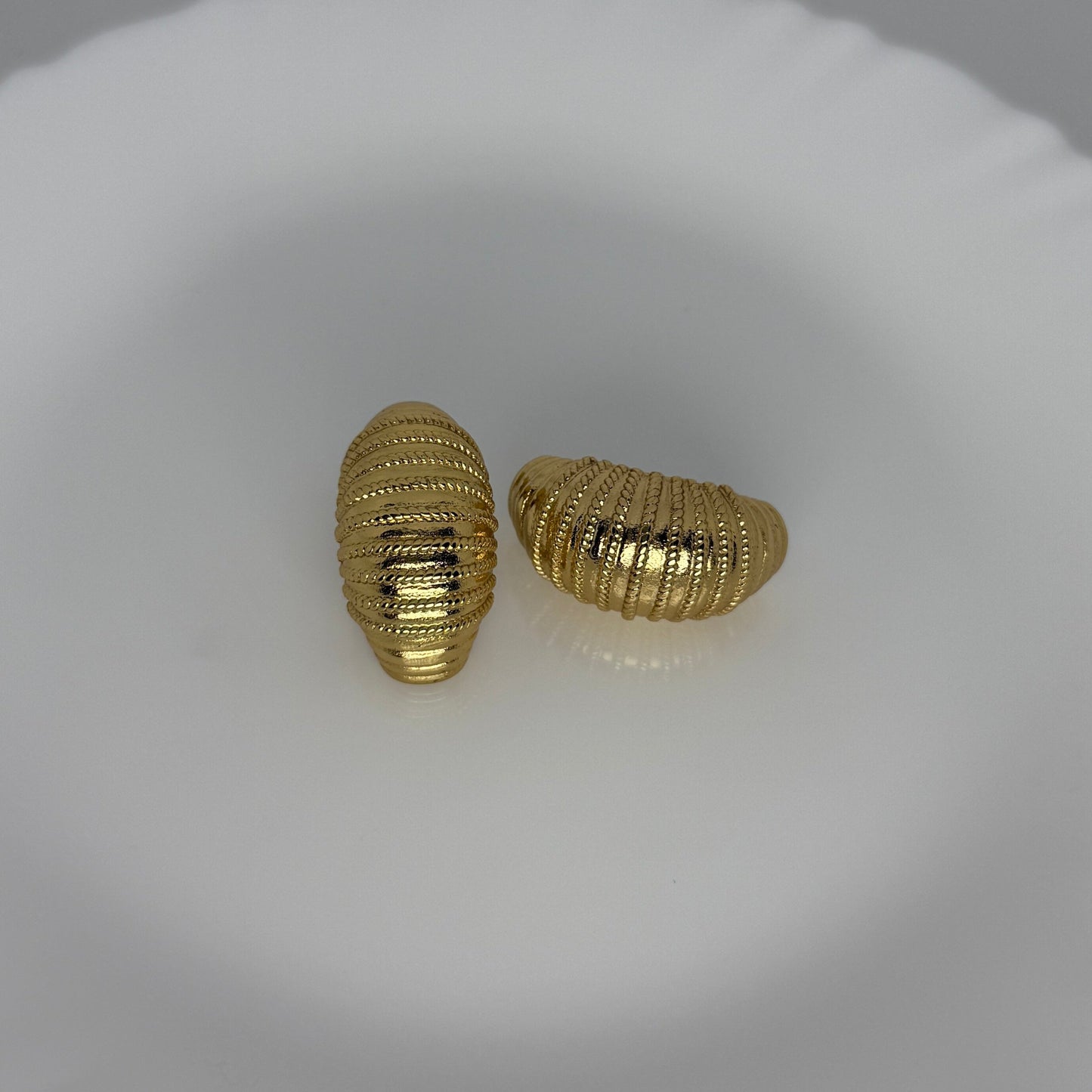 Pair of gold textured earrings on a white dish