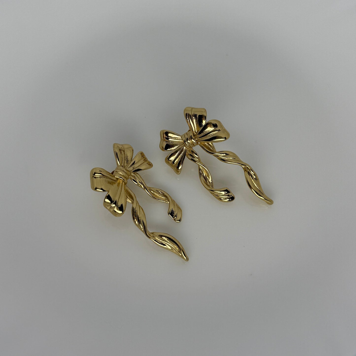 Pair of gold bow-shaped earrings on a white dish