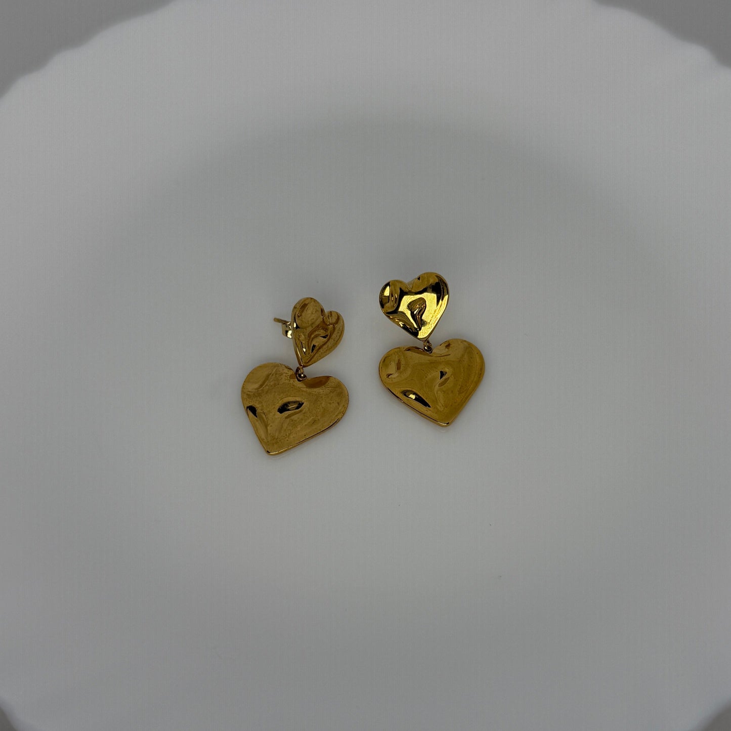 Gold heart-shaped earrings on a white dish