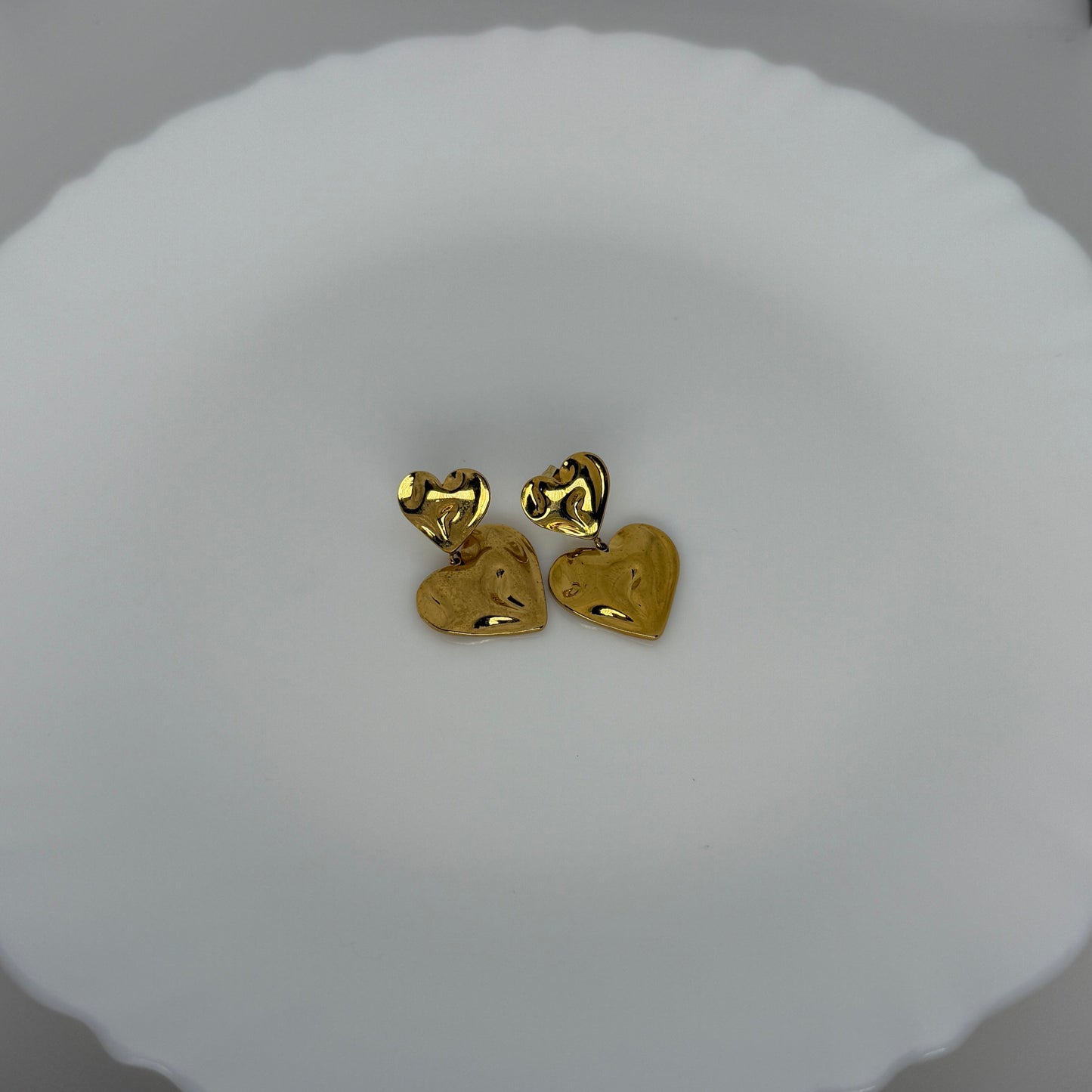 Gold heart-shaped earrings on a white cushion with a blurred background