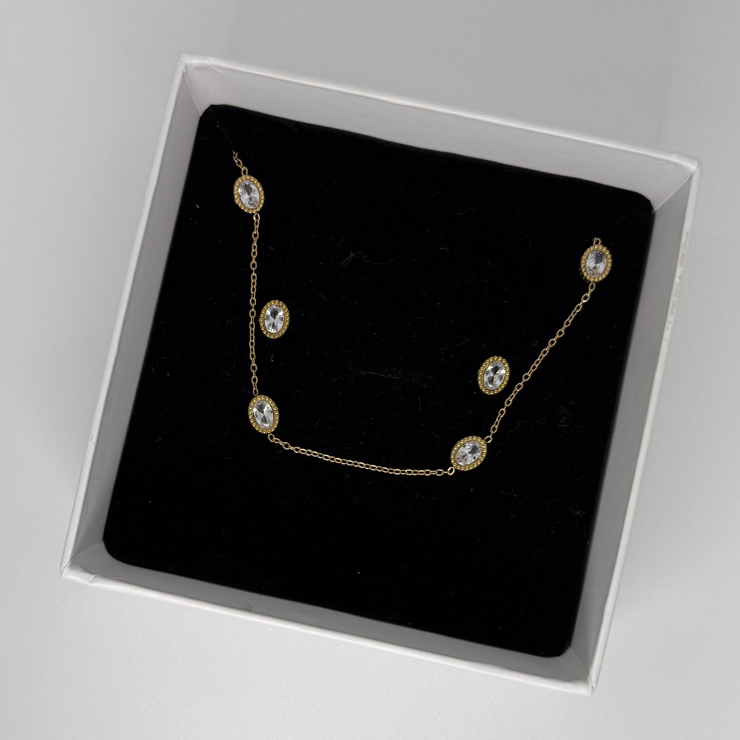 Gold necklace with clear stones in a black box on a gray background