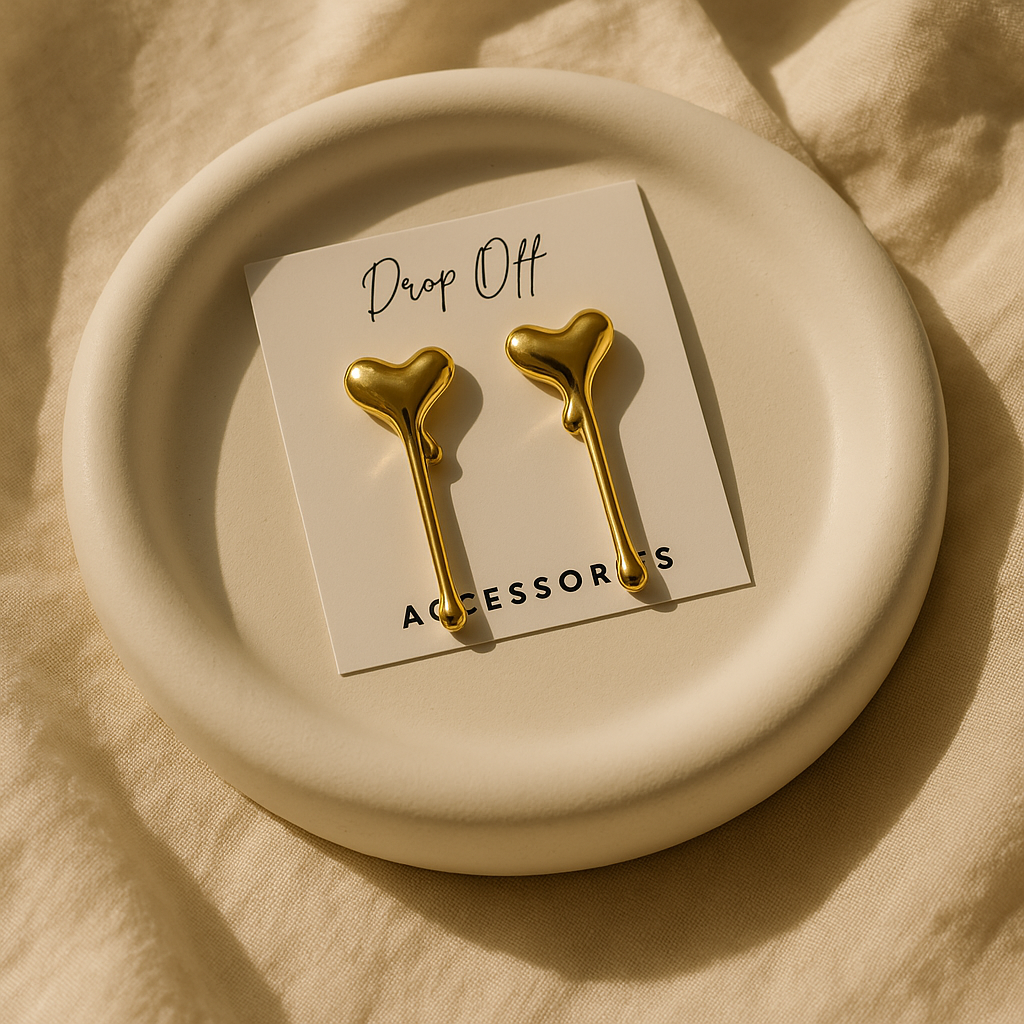 Gold heart-shaped earrings on a 'Drop Off Accessories' card on a beige plate.