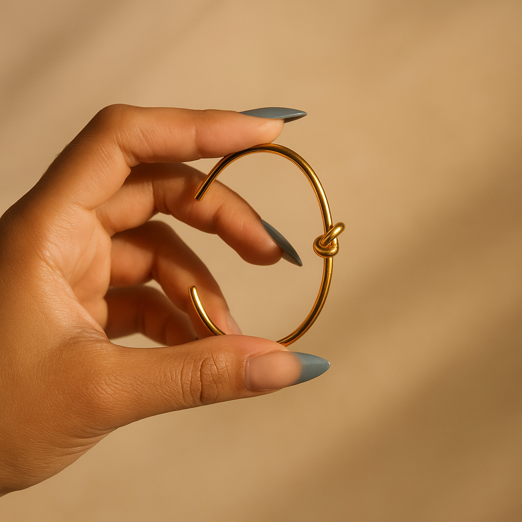 Gold hoop earring held by a hand against a beige background
