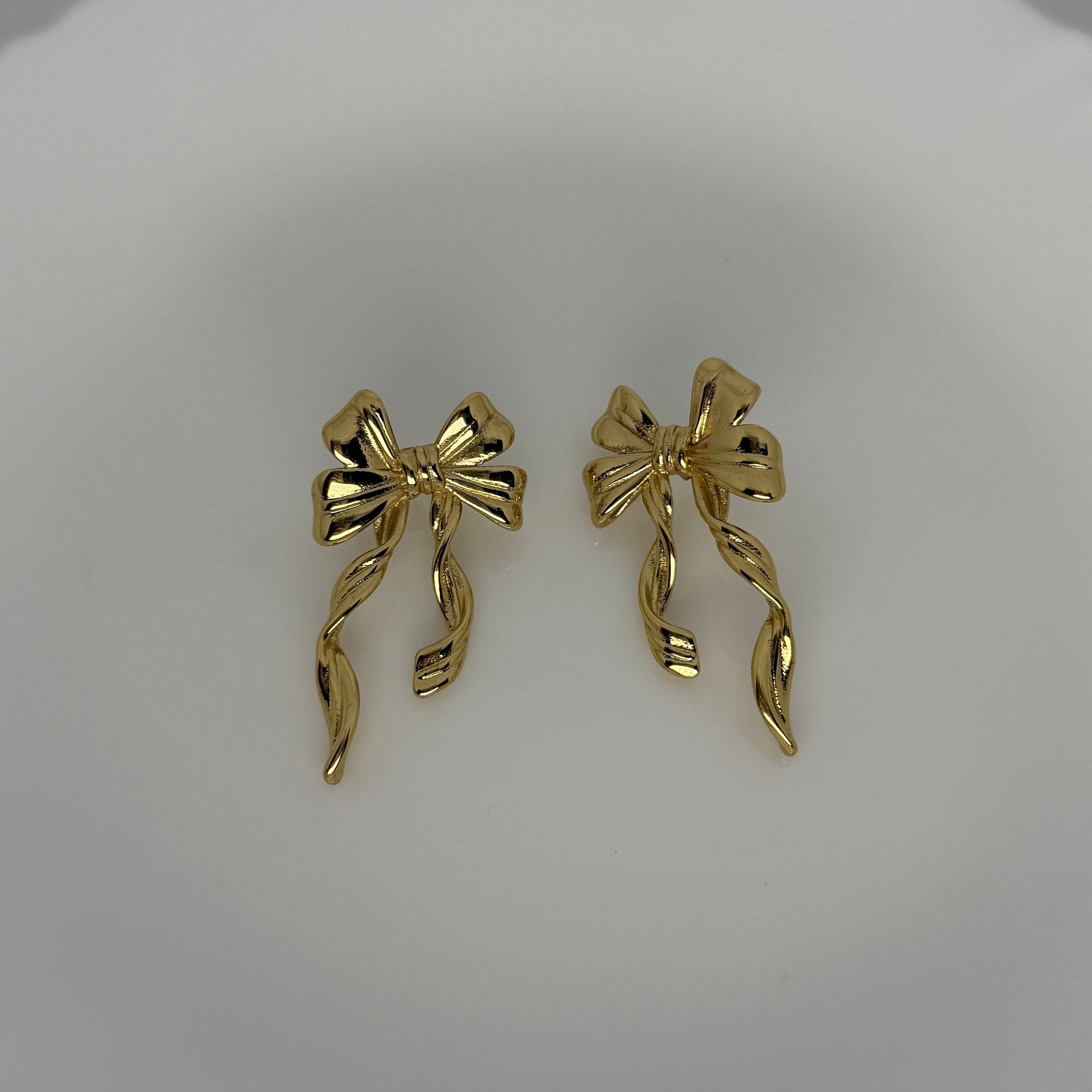 Gold bow-shaped earrings on a light gray background