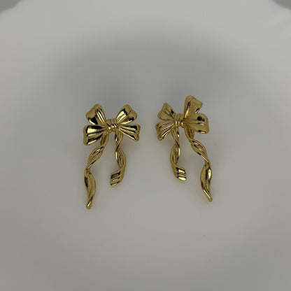 Gold bow-shaped earrings on a light gray background