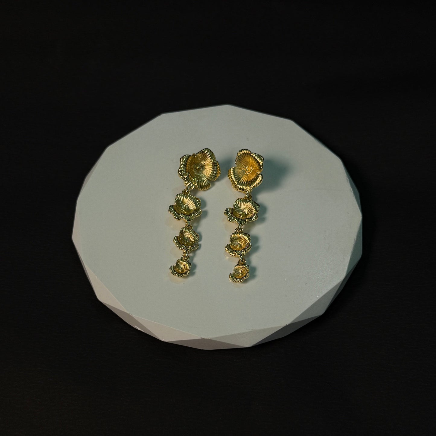 Pair of gold earrings on a white stone surface with a black background