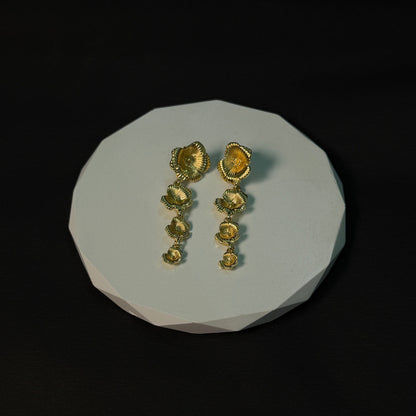 Pair of gold earrings on a white stone surface with a black background
