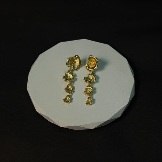 Pair of gold earrings on a white stone surface with a black background