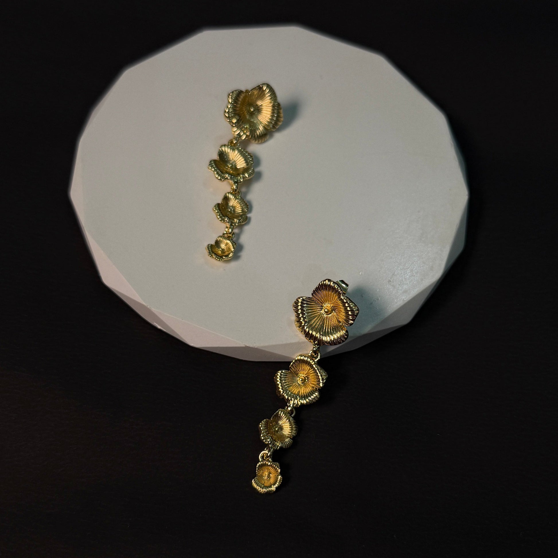 Gold earrings on a white stand against a black background