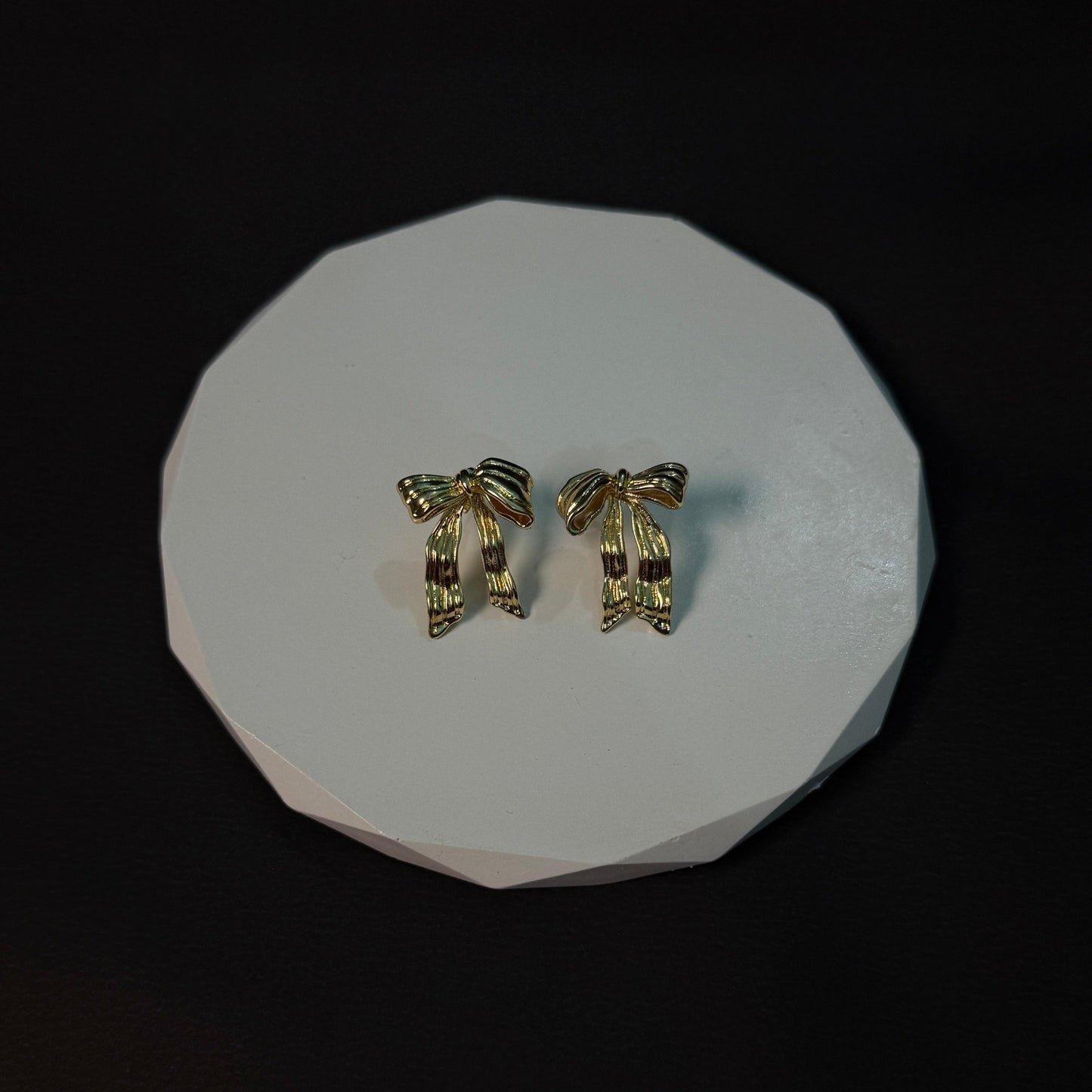 Pair of gold earrings on a white circular stand against a black background