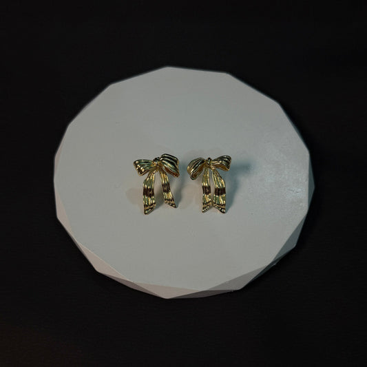 Pair of gold earrings on a white circular stand against a black background