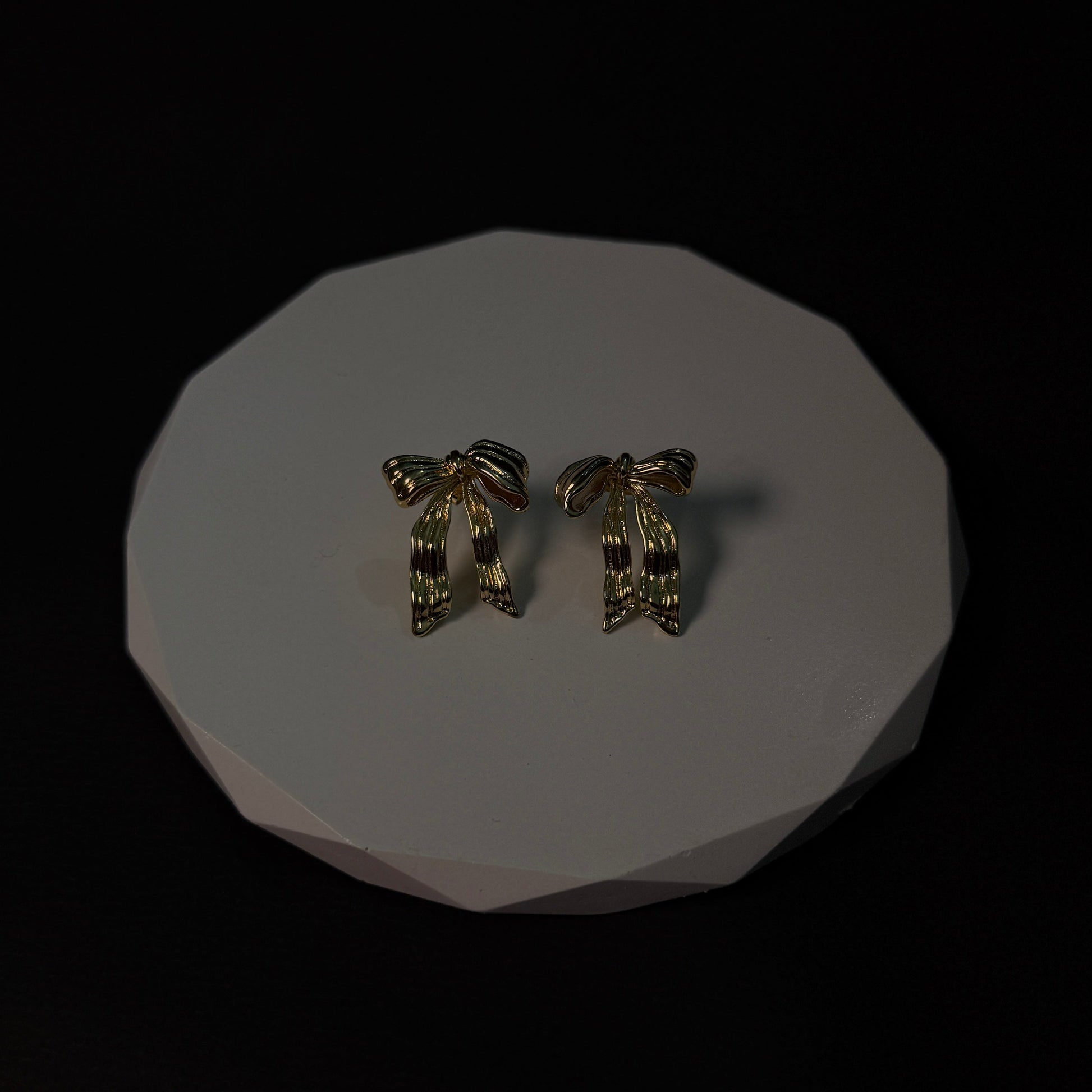 Pair of gold earrings on a white platform with a black background