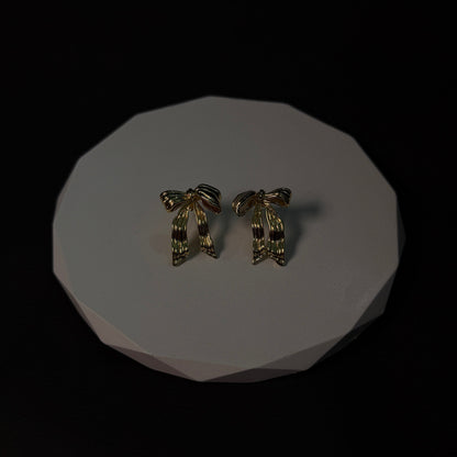 Pair of gold earrings on a white platform with a black background