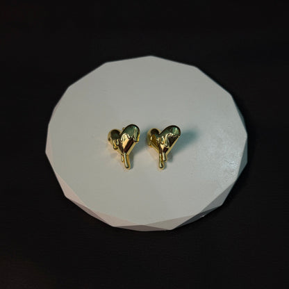 Gold heart-shaped earrings on a white stone surface with a dark background