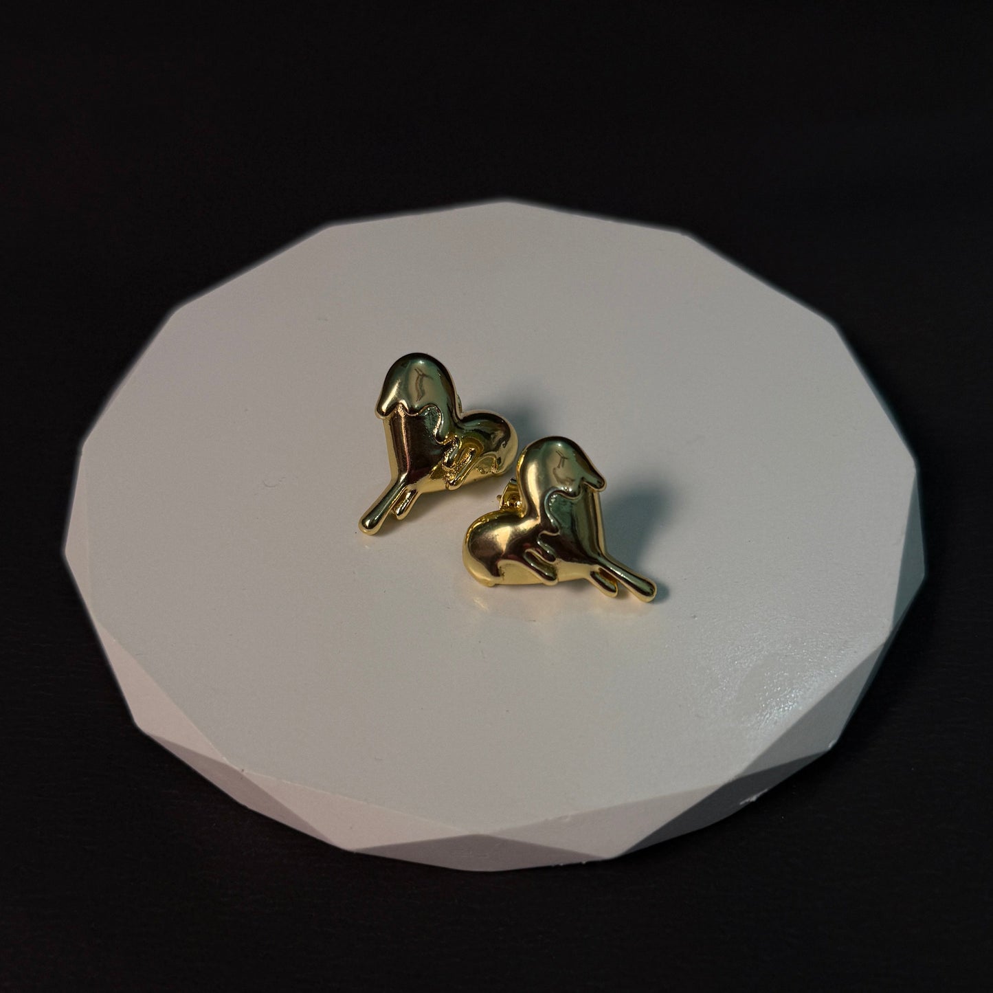 Gold bird-shaped earrings on a white stone surface with a black background