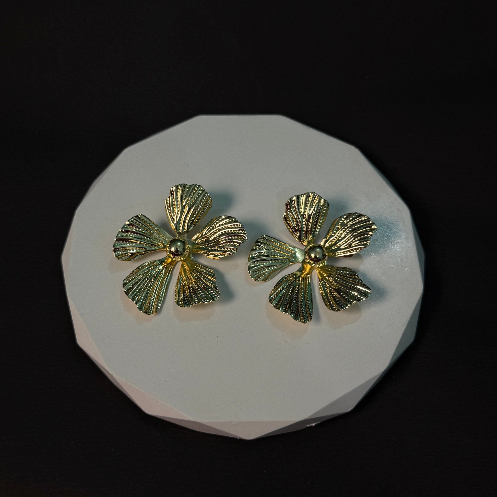 Gold flower-shaped earrings on a white platform with a black background