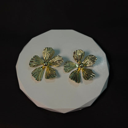 Gold flower-shaped earrings on a white platform with a black background
