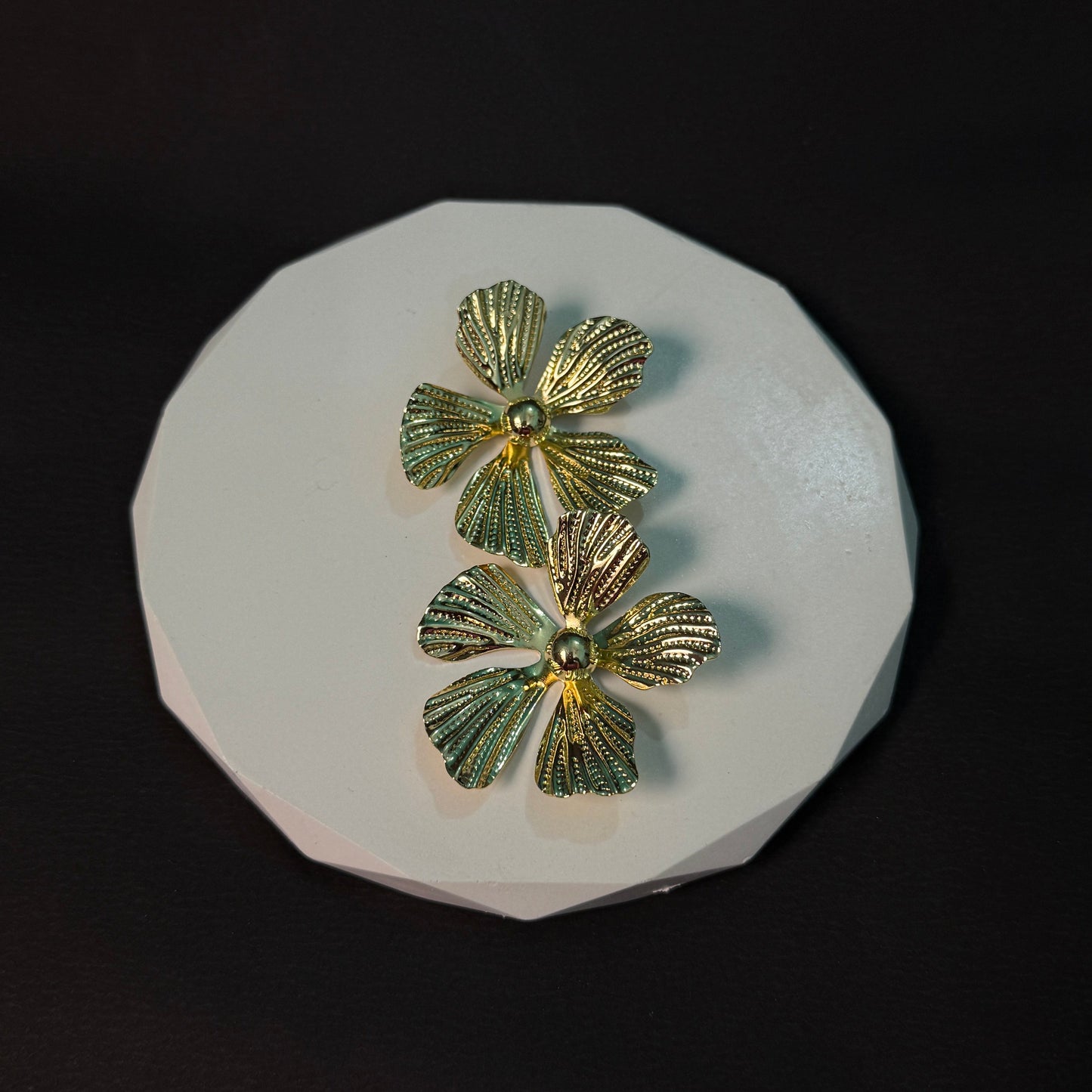 Gold and green floral earrings on a white stone surface with a black background