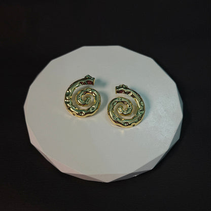Pair of gold spiral earrings on a white stand against a black background