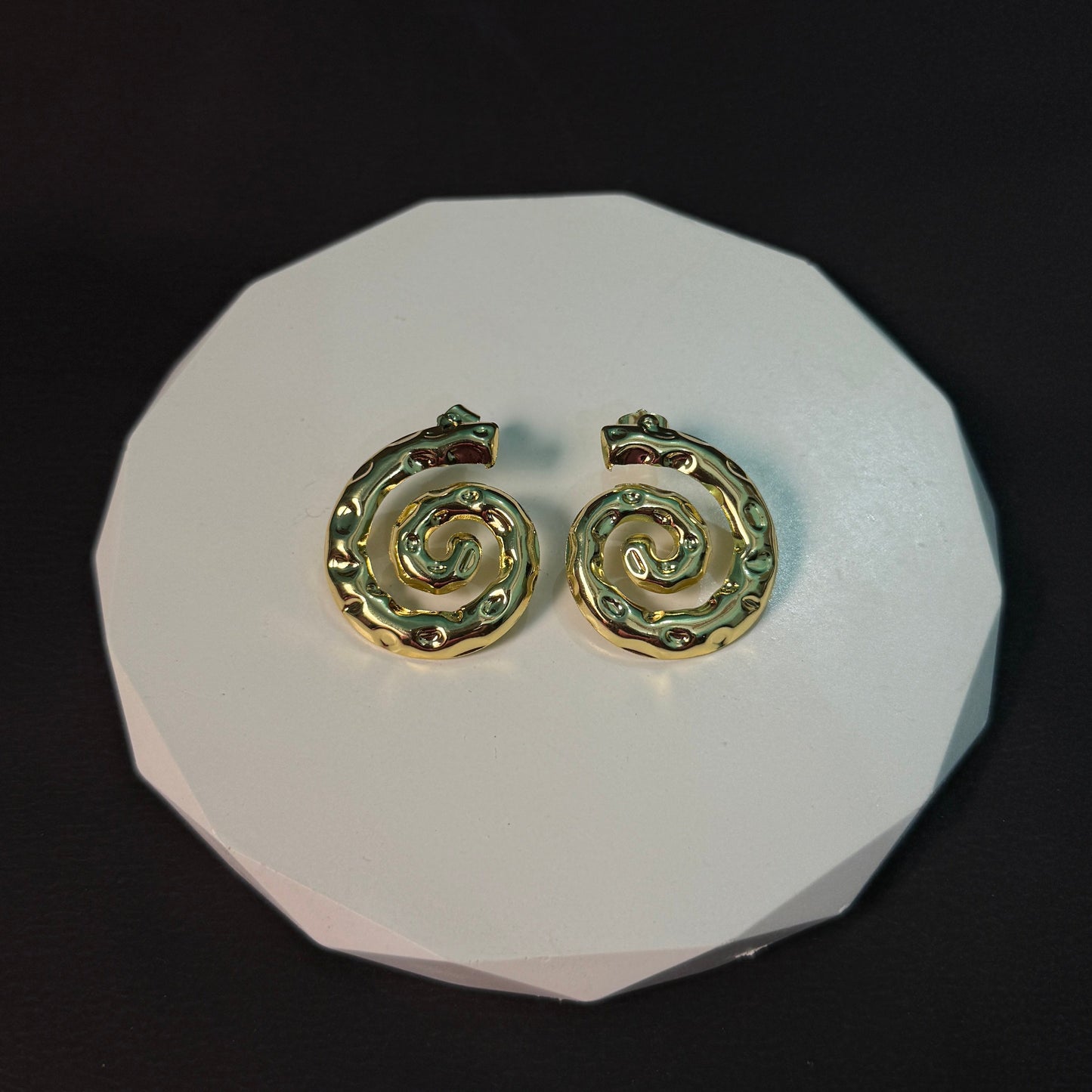 Gold spiral earrings on a white circular stand against a black background