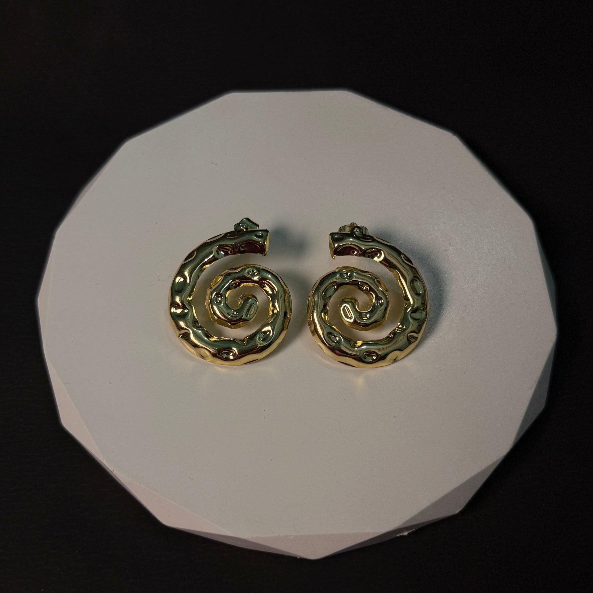 Gold spiral earrings on a white circular stand against a black background