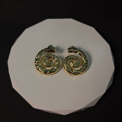 Gold spiral earrings on a white circular stand against a black background