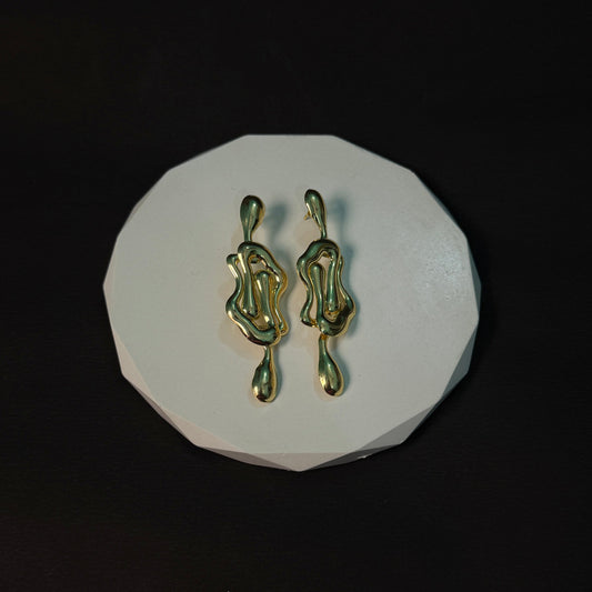 Gold earrings on a white circular pad against a black background