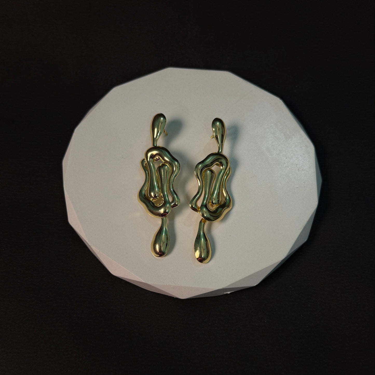 Gold earrings on a white circular stand against a black background