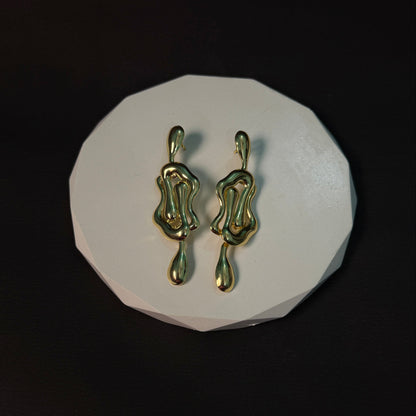 Gold earrings on a white circular stand against a black background