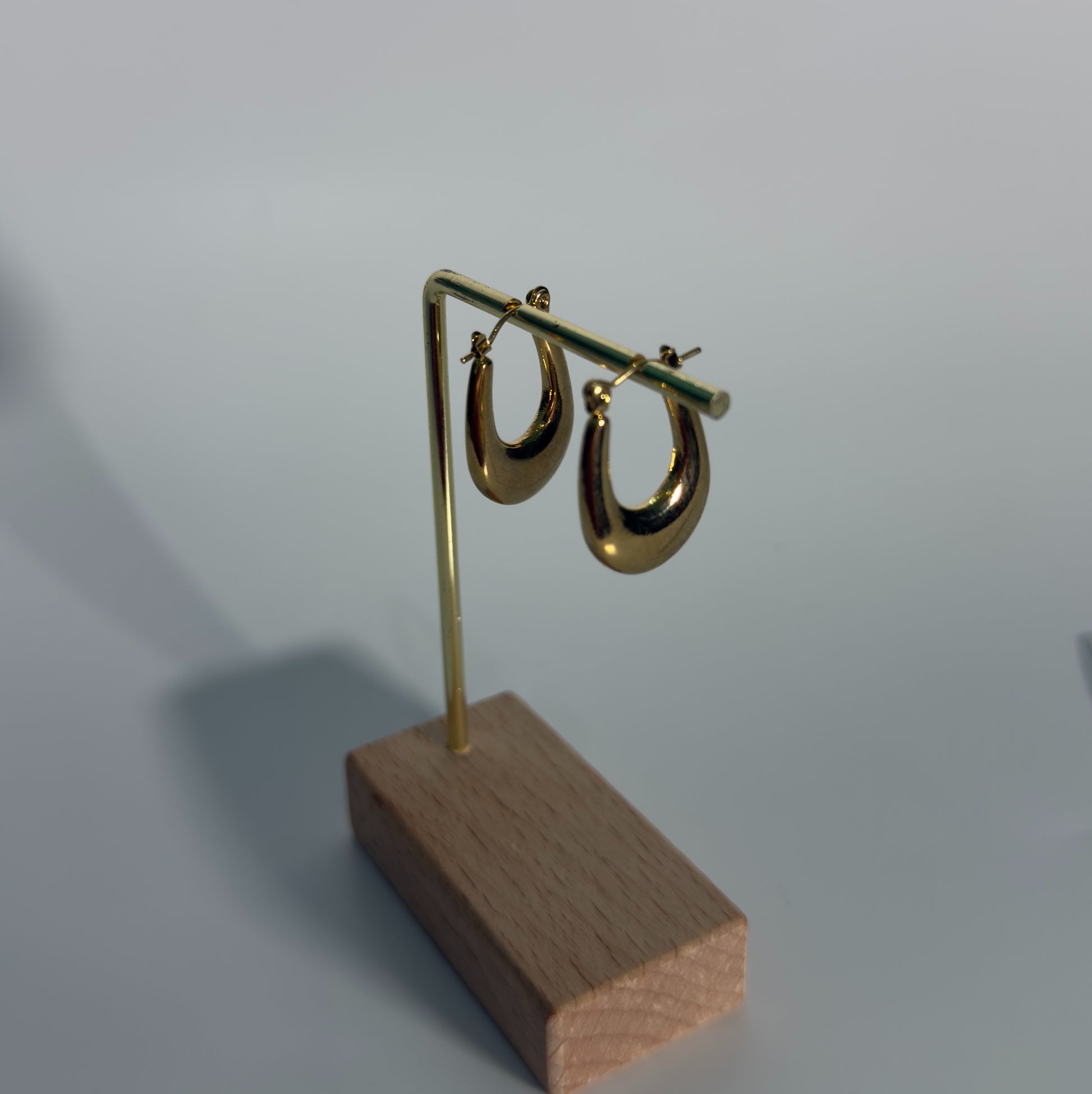 Gold hoop earrings on a wooden stand against a light gray background