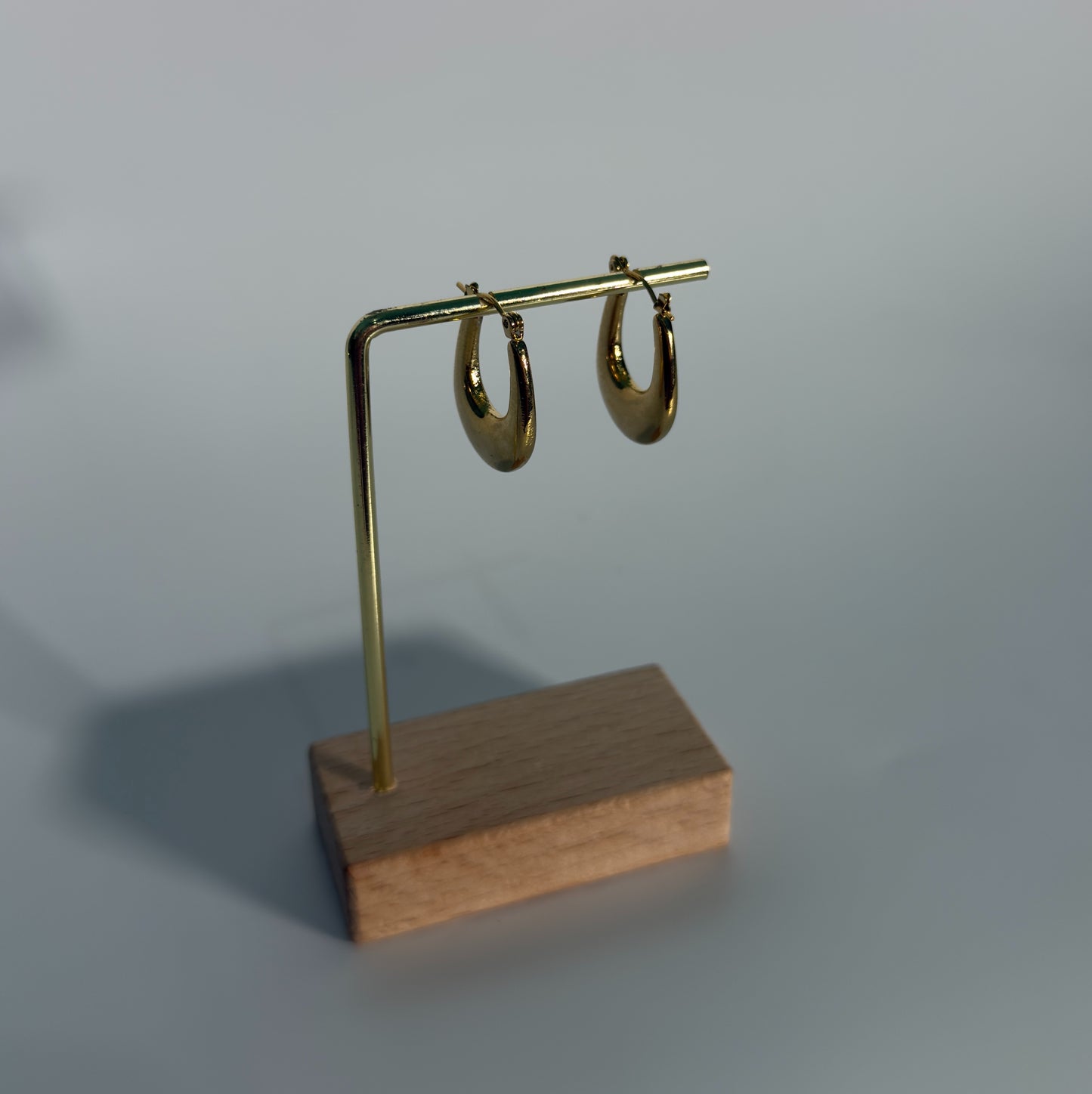 Gold hoop earrings on a wooden stand against a gray background