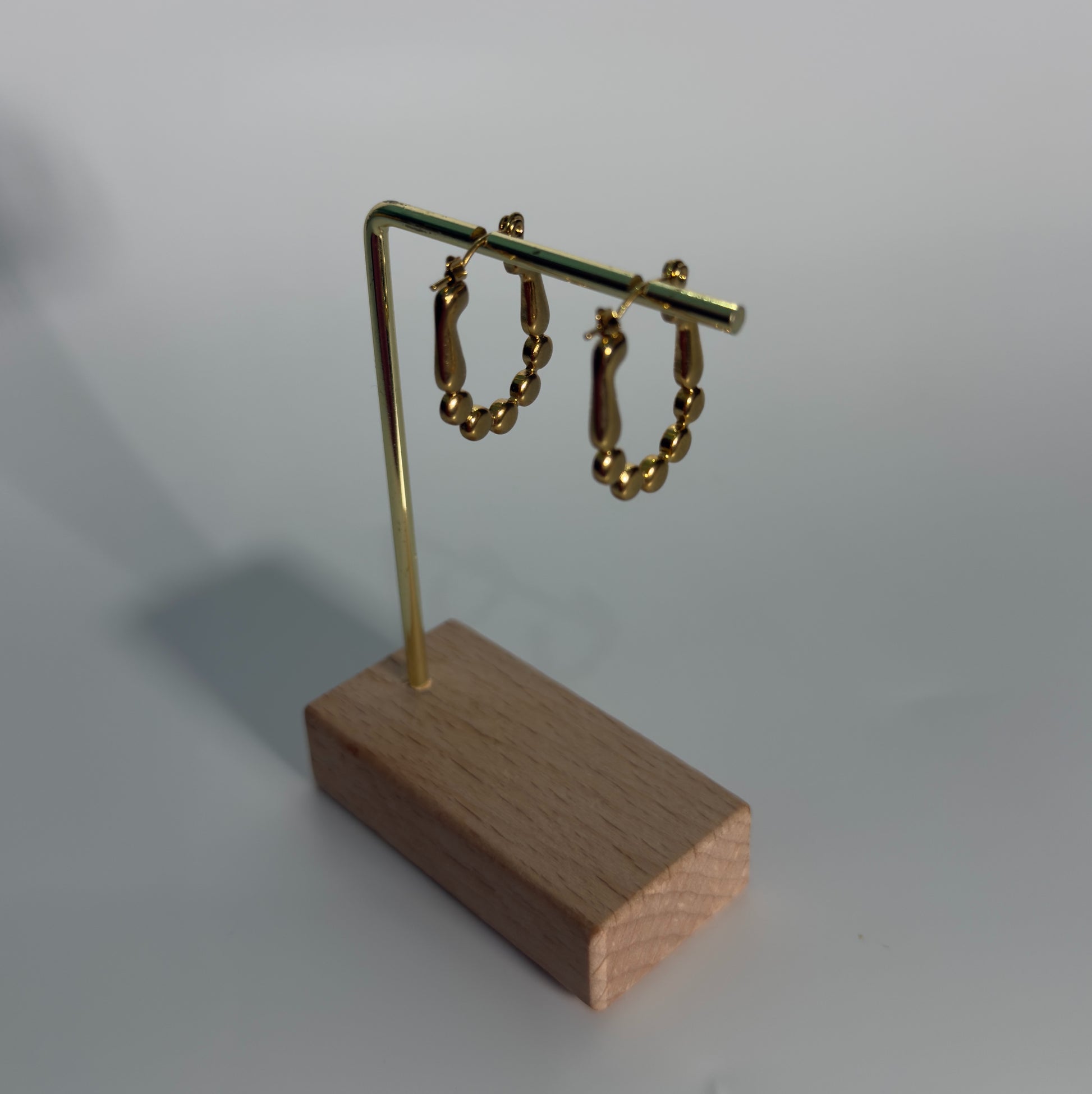 Gold hoop earrings on a wooden stand against a gray background