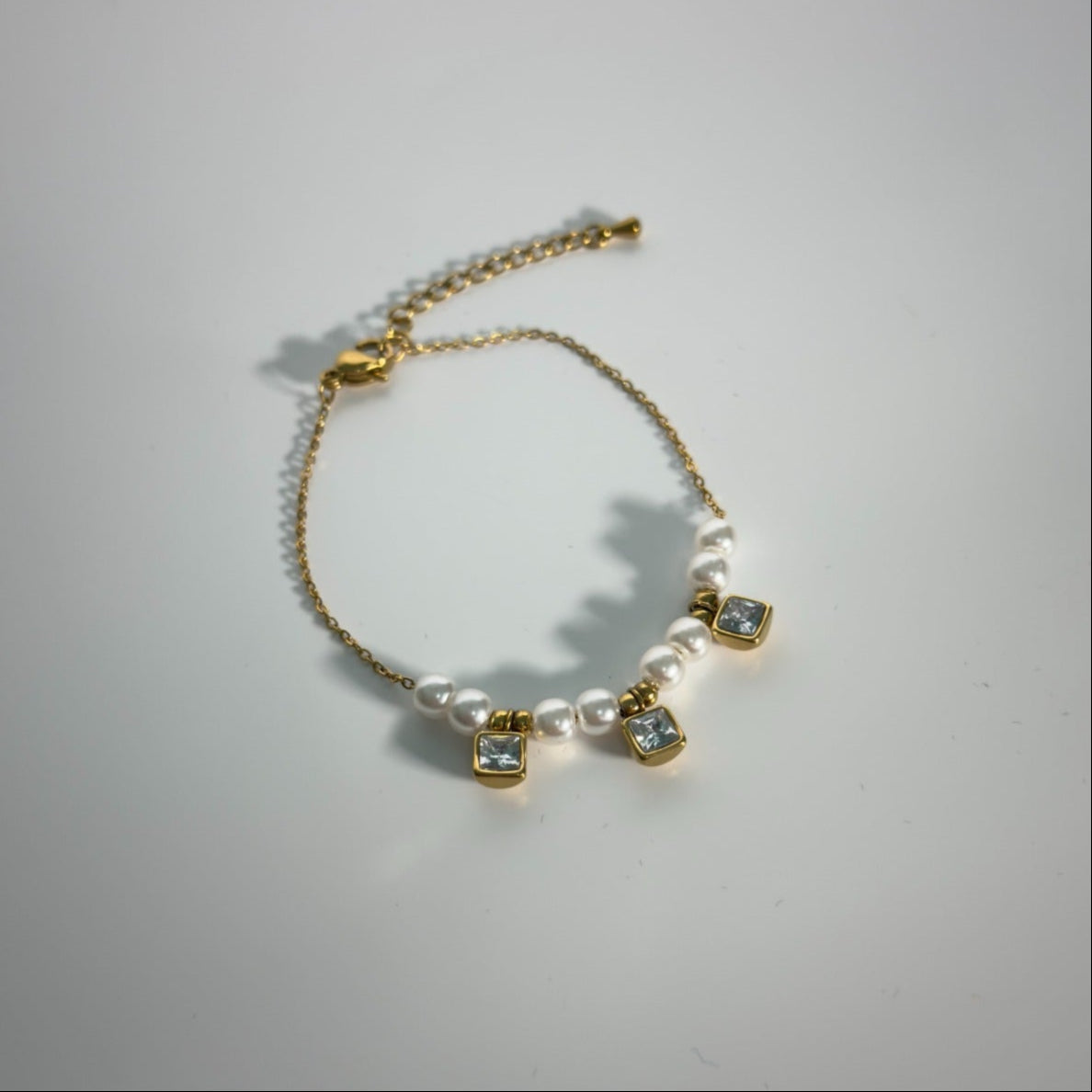 Gold bracelet with pearls and gemstones on a light gray background