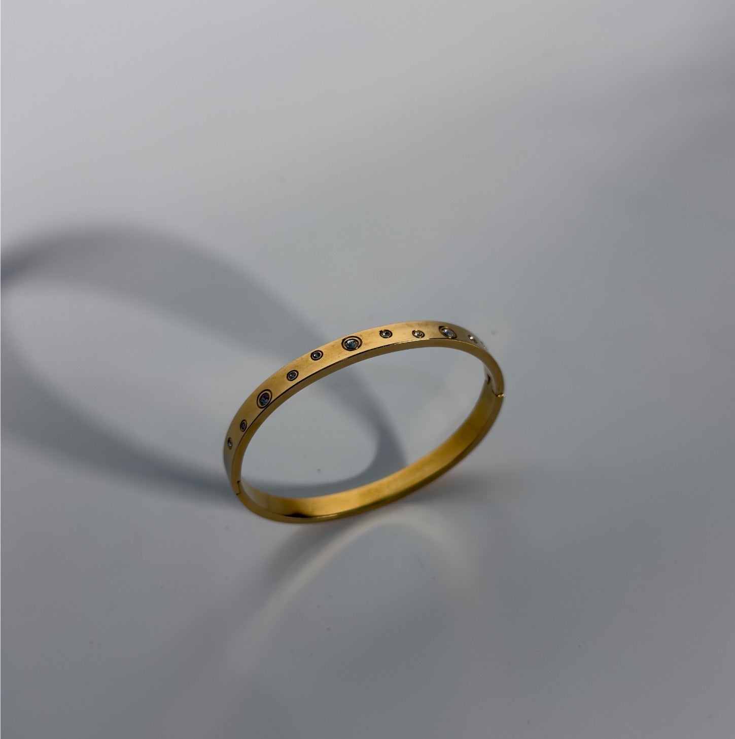 Gold bracelet with small stones on a gray background