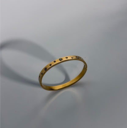 Gold bracelet with small stones on a gray background