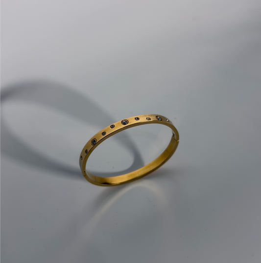 Gold bracelet with small stones on a gray background