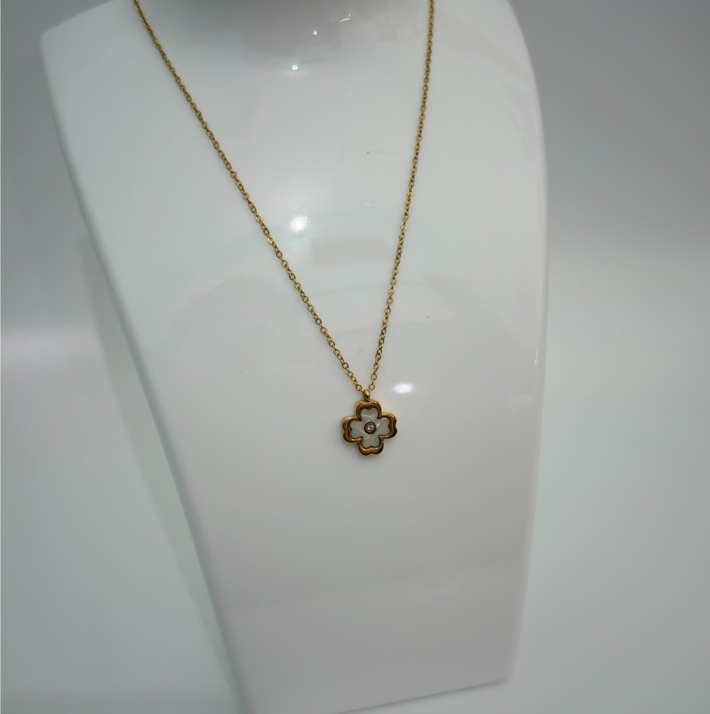 Gold necklace with a floral pendant on a white mannequin bust.