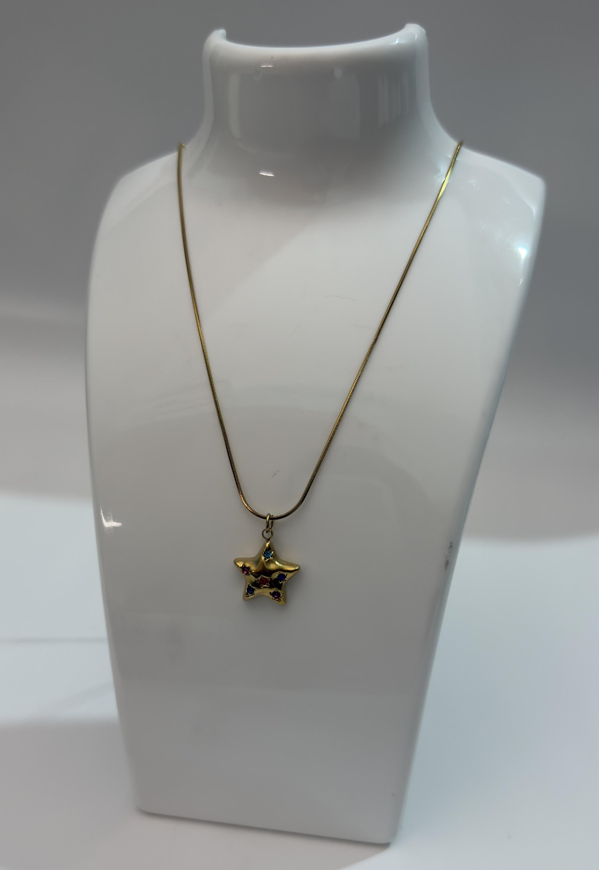Gold necklace with a star-shaped pendant on a white mannequin bust.