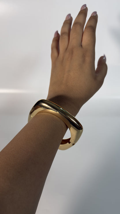Gold bracelet on a wrist against a white background