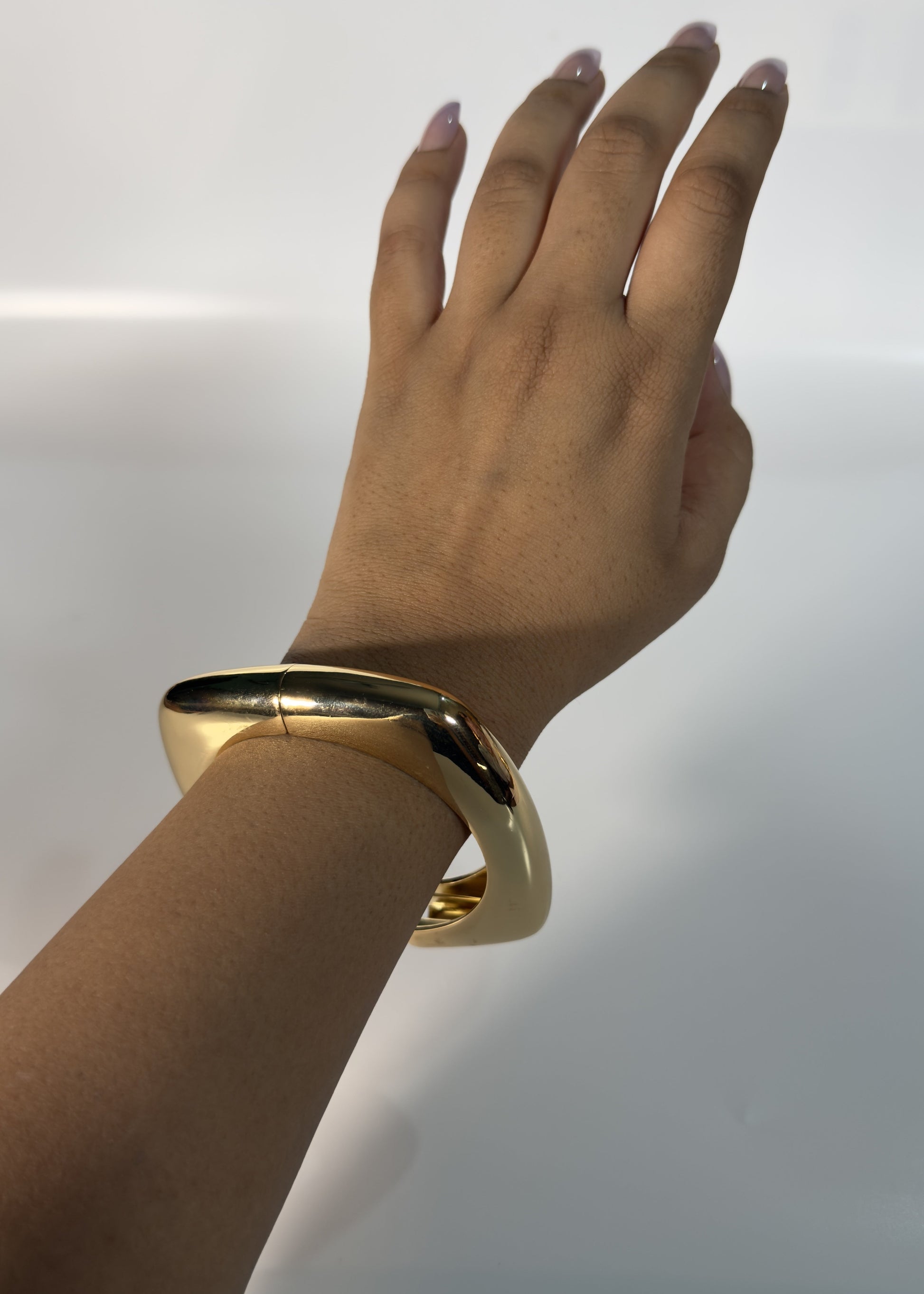Hand wearing a gold bracelet against a light background