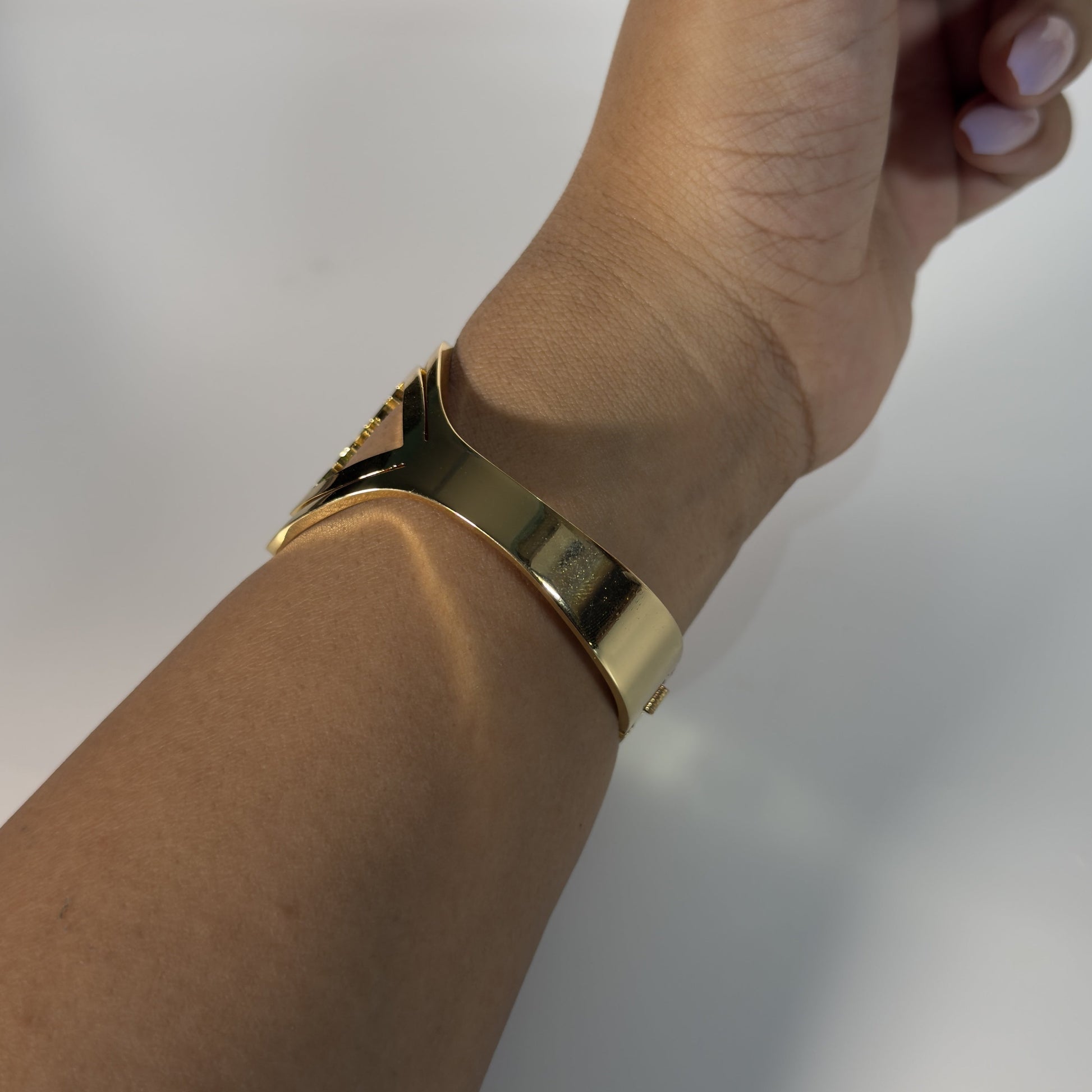 Hand wearing a gold bracelet on a plain background